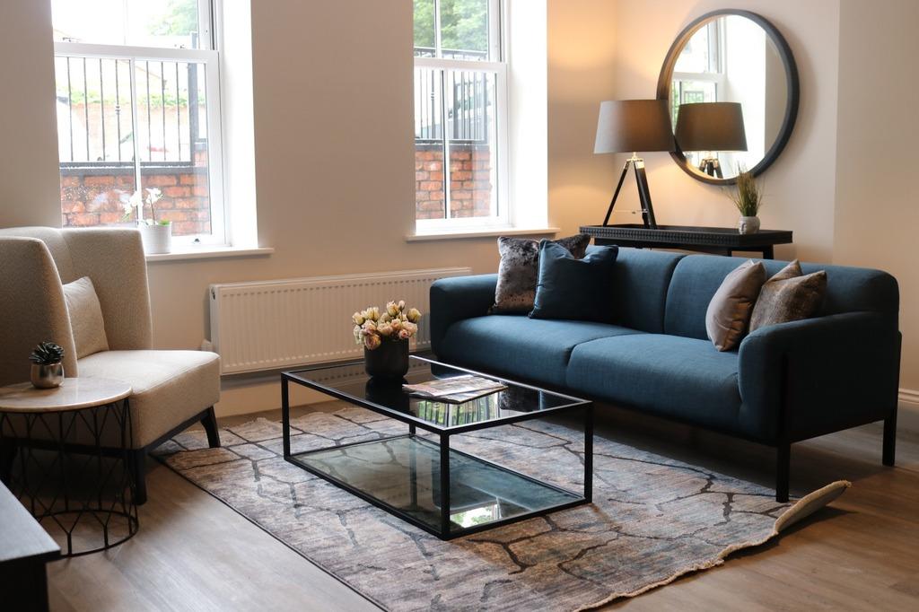 a living room, with navy sofa, patterned rug, glass coffee table, and light coloured armchair