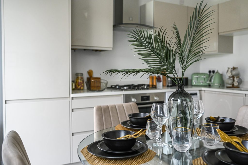 a white, modern kitchen and a glass dining table with a vase of foliage in the centre