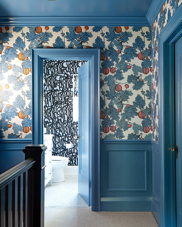 air force blue, half height panelling in a hallway with cole and son wallpaper above, showing oranges, blue leaves, and small monkeys hidden throughout