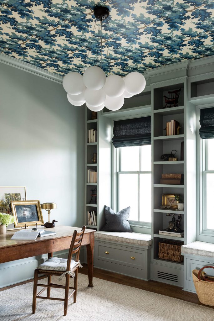 an office space painted in a light turquoise colour with a bold, foliage print wallpaper on the ceiling