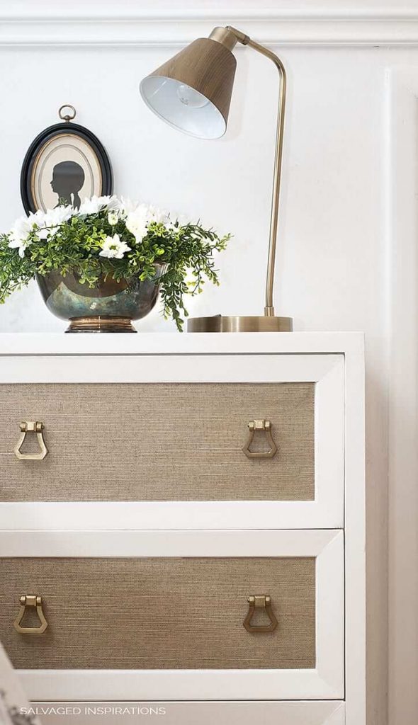 a small chest of drawers with a neutral, woven texture wallpaper inset into the drawer fronts 