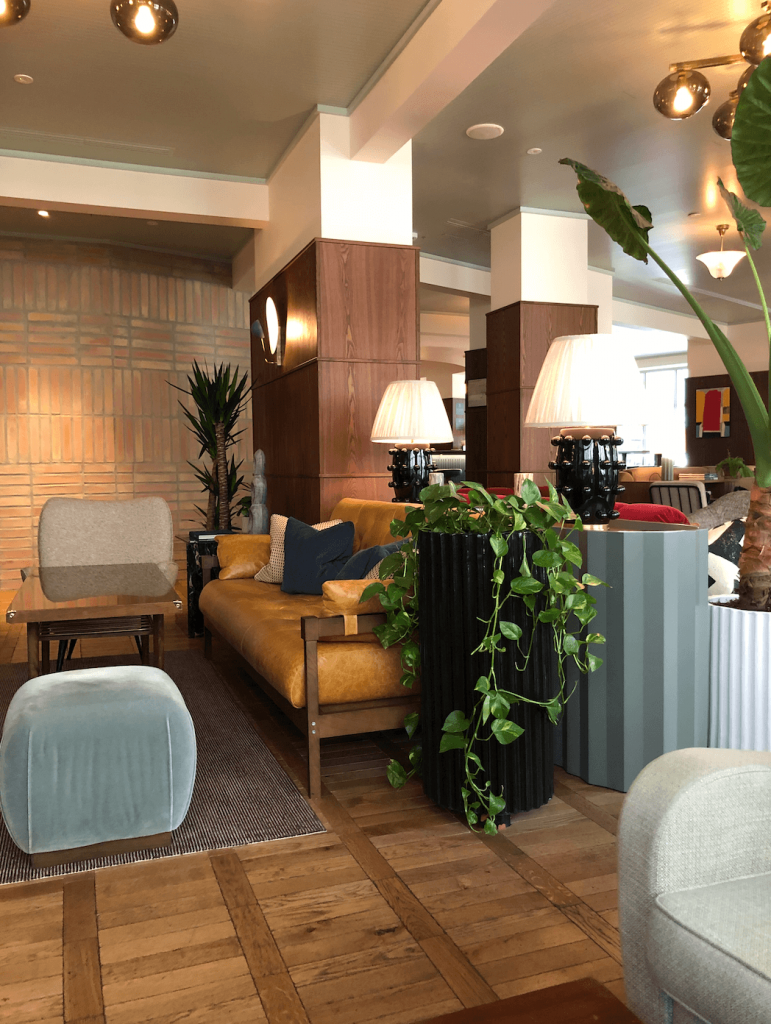 hoxton hotel lobby. A seating area with ochre sofa, planters with foliage, and various lighting