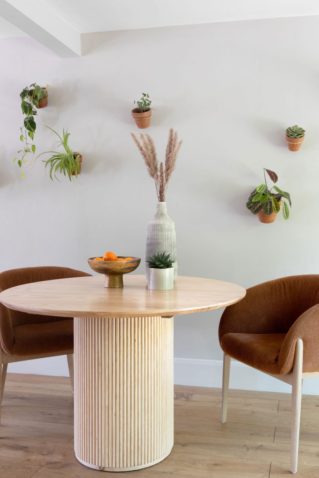 wooden round dining table, fluted table base, plant wall, ribbed fabric chairs, upholstered dining chairs, terracotta interior