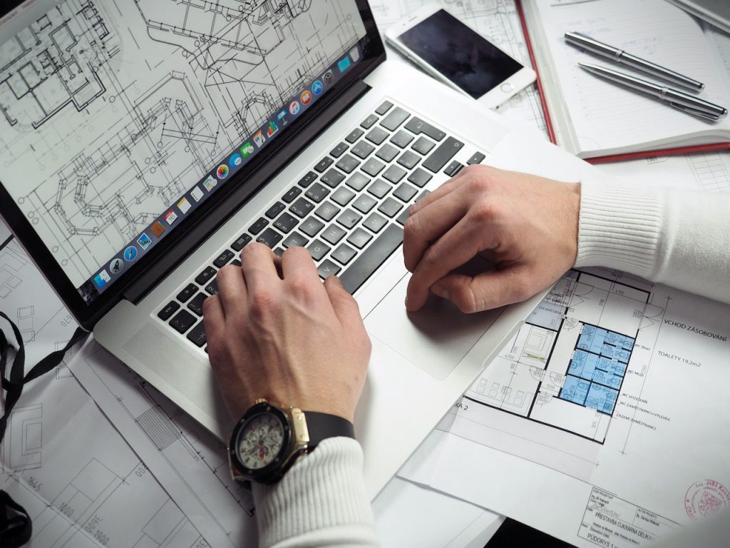 photo of a person editing floor plans on a laptop, with more plans surrounding them on the desk