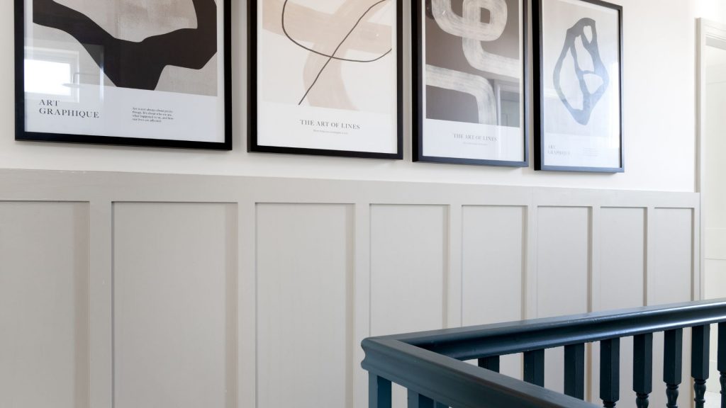 A close up of a landing with pastel painted wall panelling, and a contrasting blue banister.