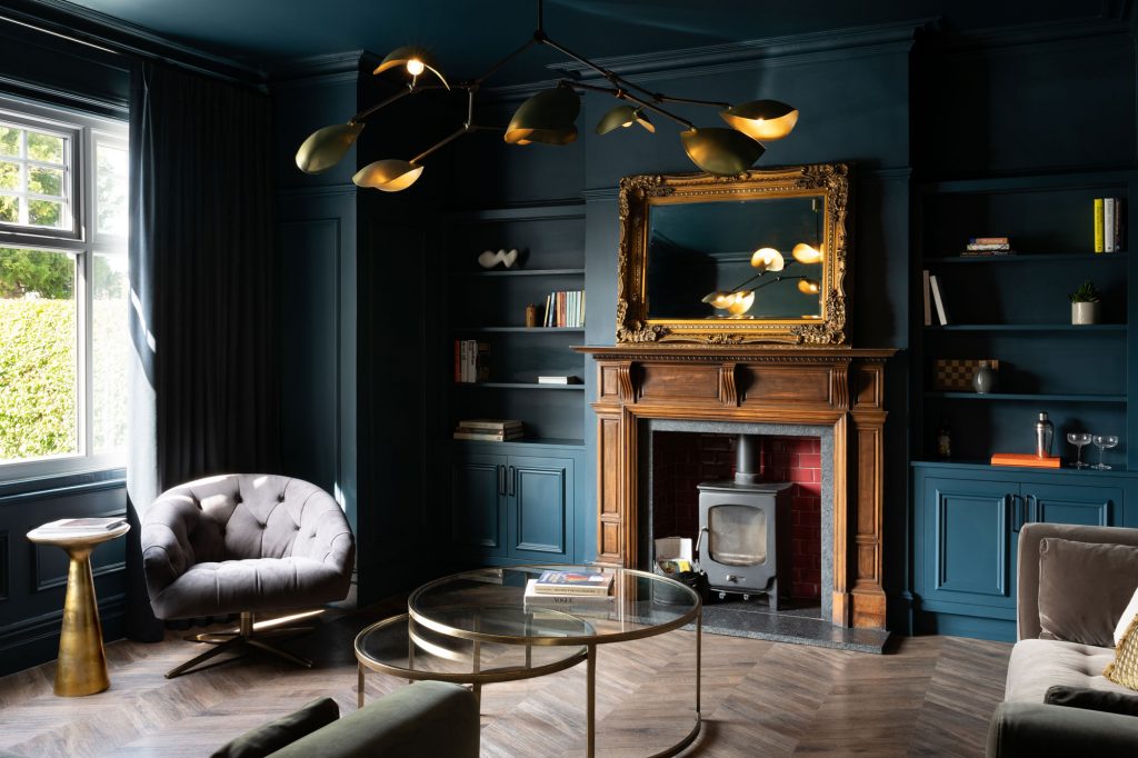 Sophisticated teal living room with gold accents and wooden fireplace demonstrating the use of deep colour to create mood and depth.