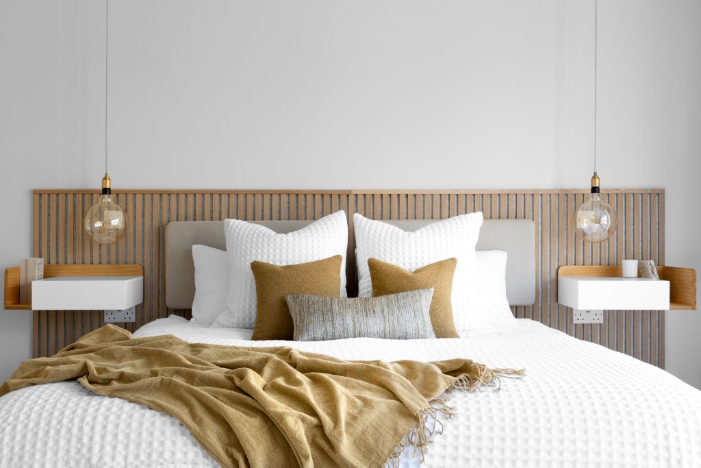 Modern bedroom with mustard-toned cushions and wooden slatted headboard showing how colour psychology creates a restful atmosphere.