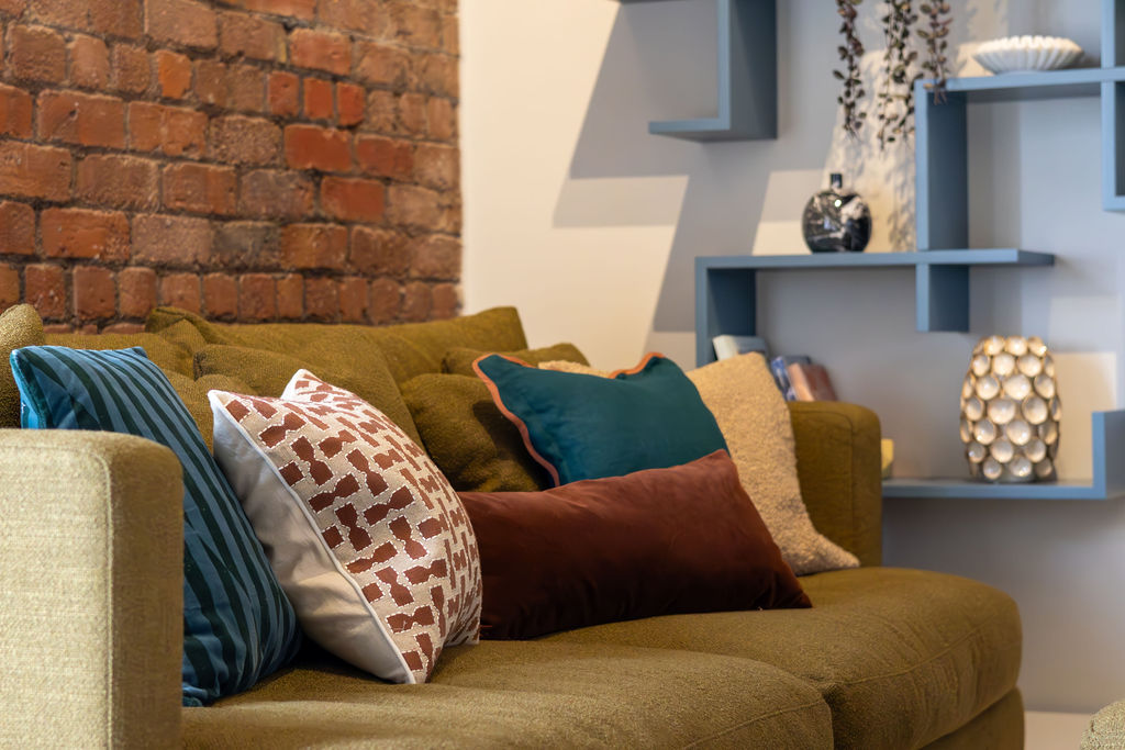 Olive sofa styled with layered cushions in teal, terracotta and rust tones showing how colour and texture add warmth and personality.