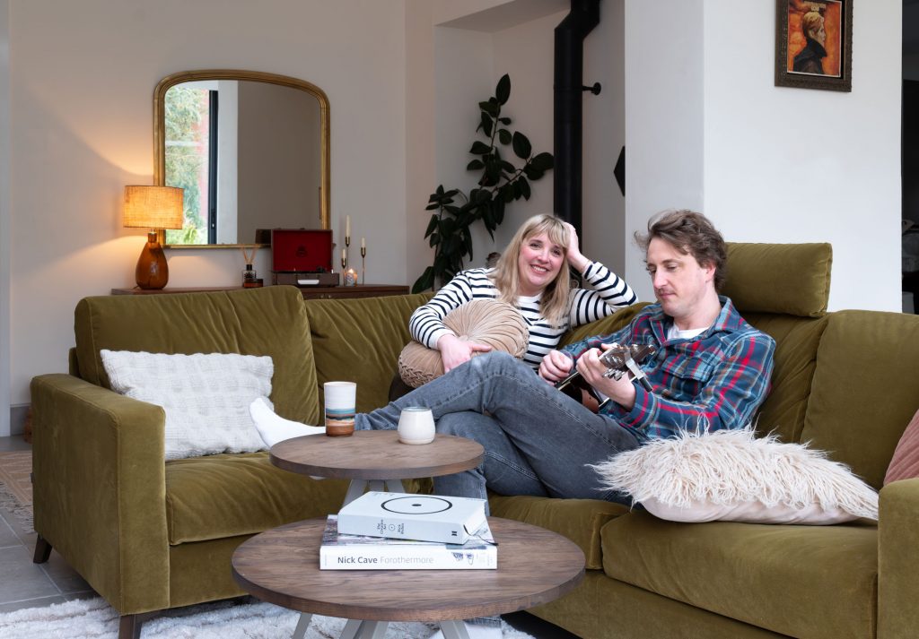 Couple relaxing on an olive-green velvet sofa with warm lighting and earthy tones reflecting a calm, balanced interior design.