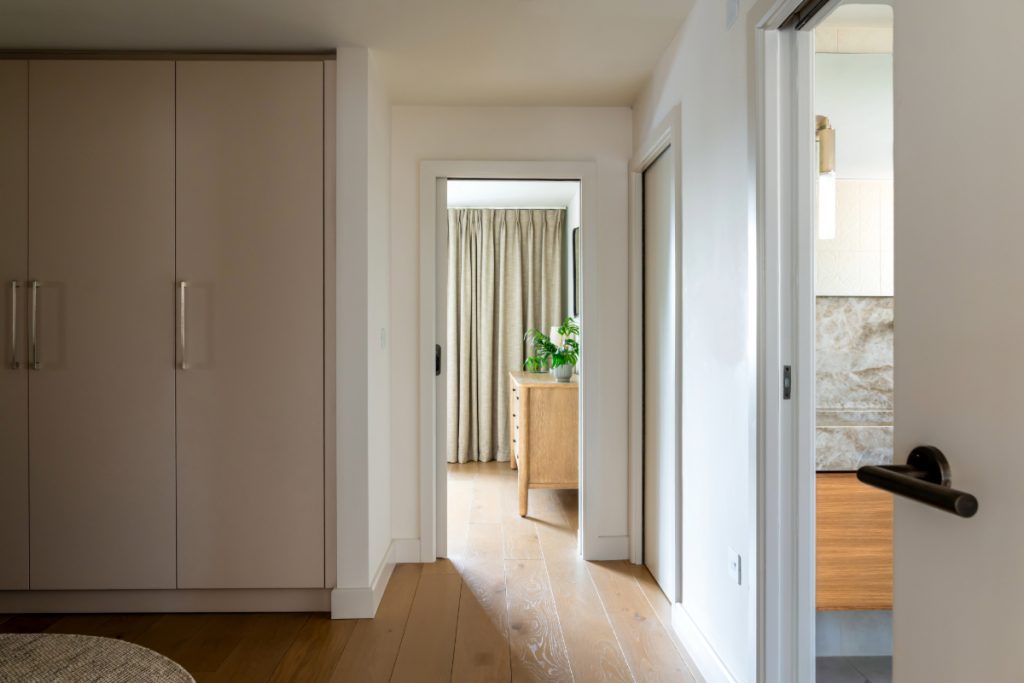 Light hallway with warm wooden floors, pale walls, and soft daylight flowing through adjoining rooms — demonstrating how continuity of colour and texture helps brighten darker areas.
