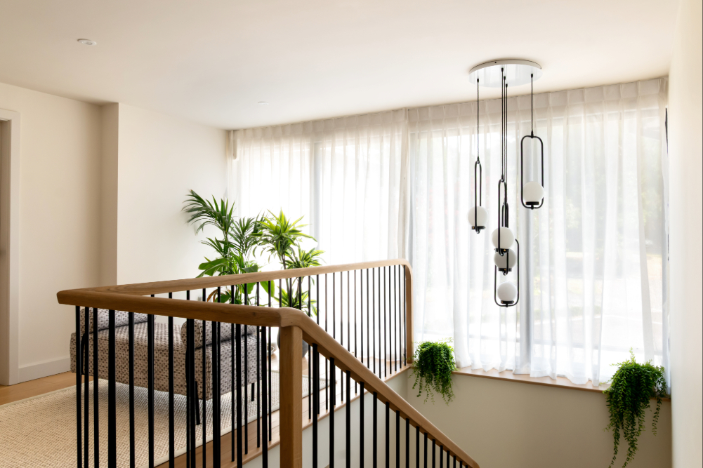 Bright landing area with sheer curtains, hanging pendant lights, and greenery illuminated by natural light — showing how soft fabrics and layered lighting enhance a room’s brightness.