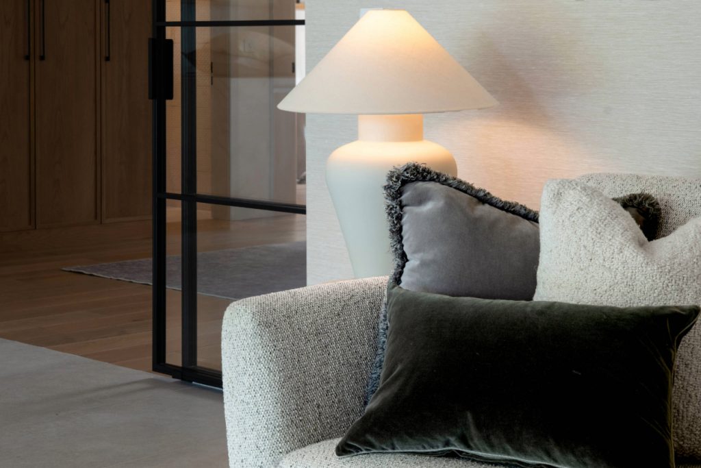 Close-up of a textured neutral armchair with layered cushions and a sculptural ceramic table lamp, showcasing calm, liveable luxury interior design in a contemporary Cheshire home.