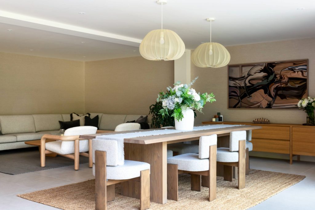Open-plan dining and living space in a contemporary Cheshire home, featuring a solid wood dining table, neutral textures and layered lighting designed for relaxed, liveable luxury.