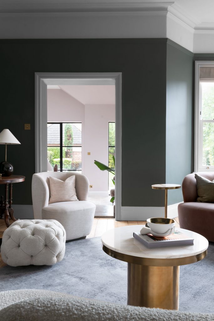 Cosy living room in a Cheshire home with deep green walls, sculptural armchairs and brass coffee table, creating a calm and characterful luxury interior.